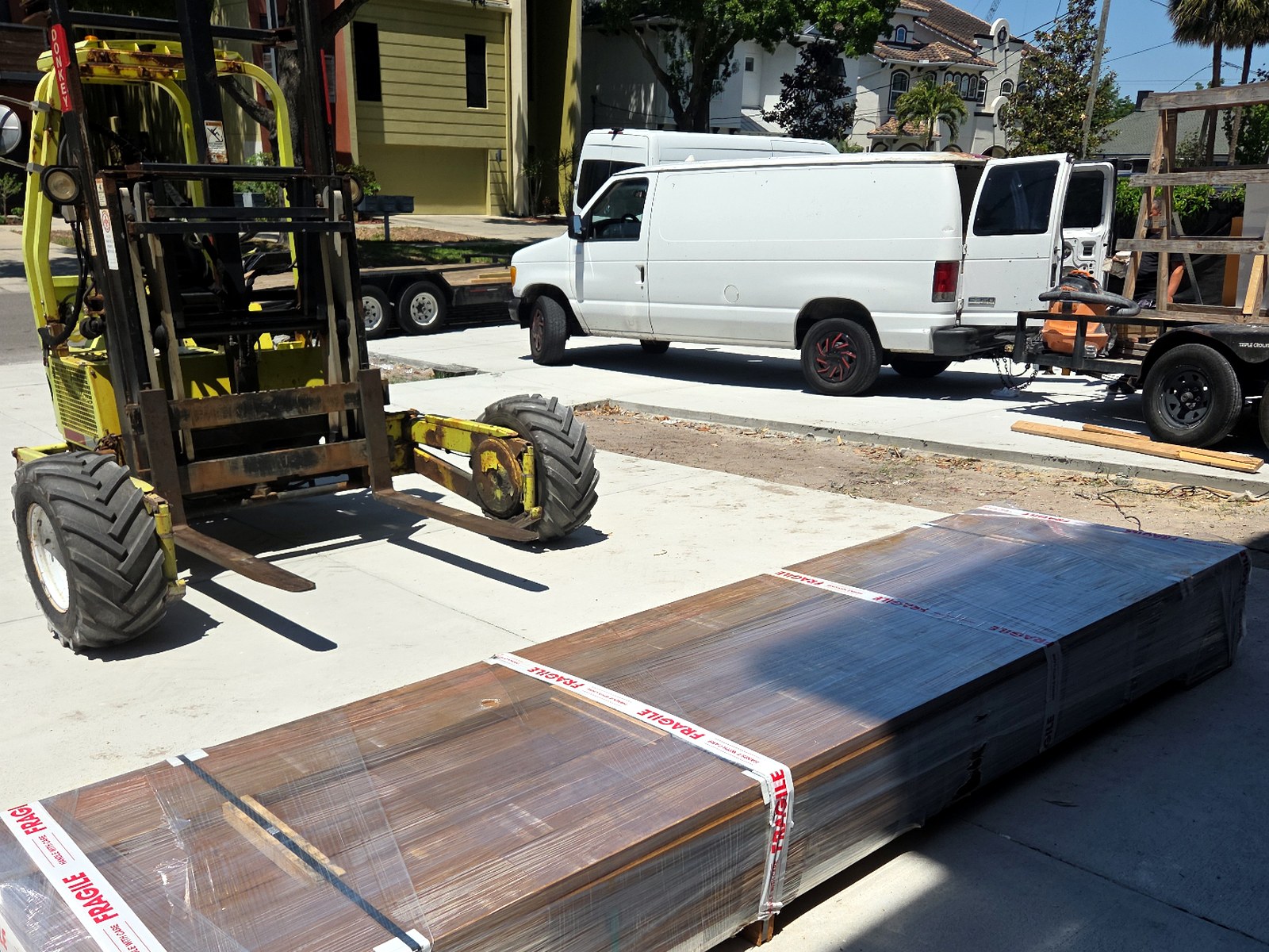 On-board forklift offloading a long pallet of wood materials on a tight urban street