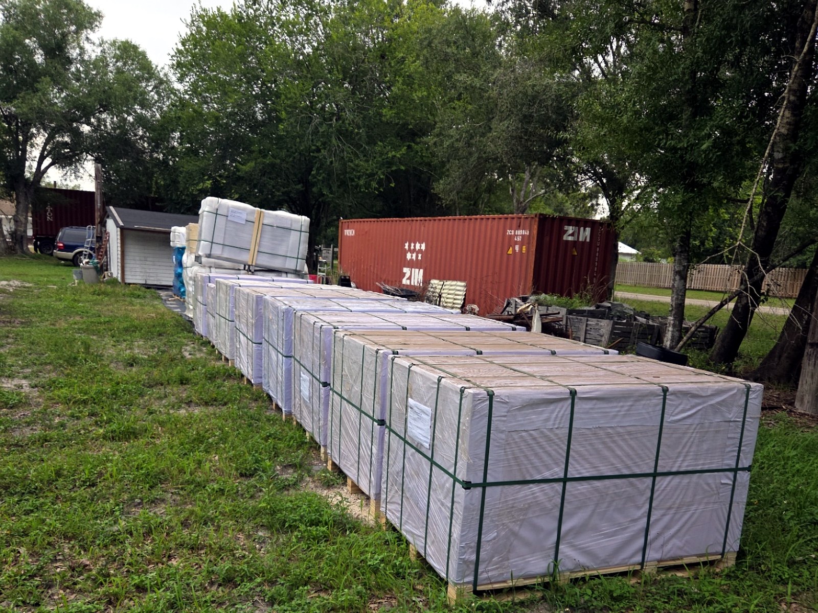 Long row of wrapped pallets staged on a jobsite yard after forklift offload