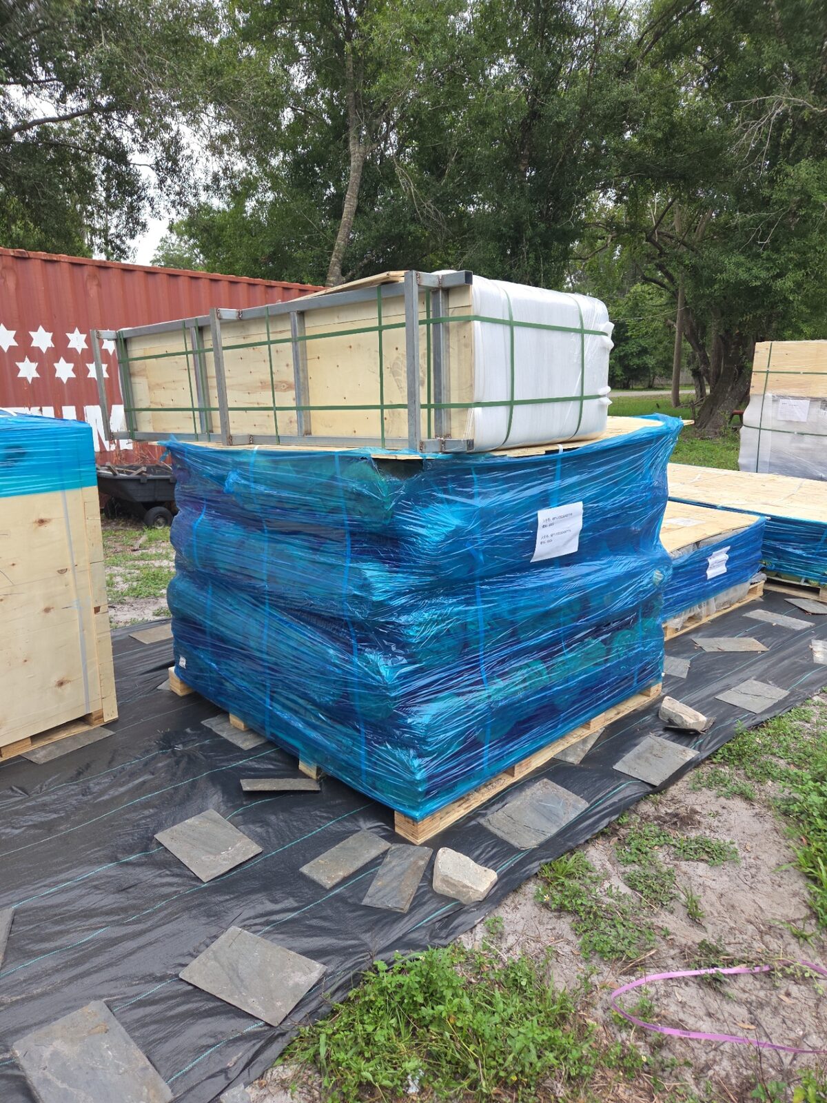 Stack of pallets wrapped in heavy blue shrink film staged on a jobsite ground cover