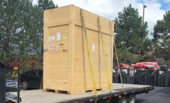 Large wooden crate strapped to a flatbed truck in a parking lot