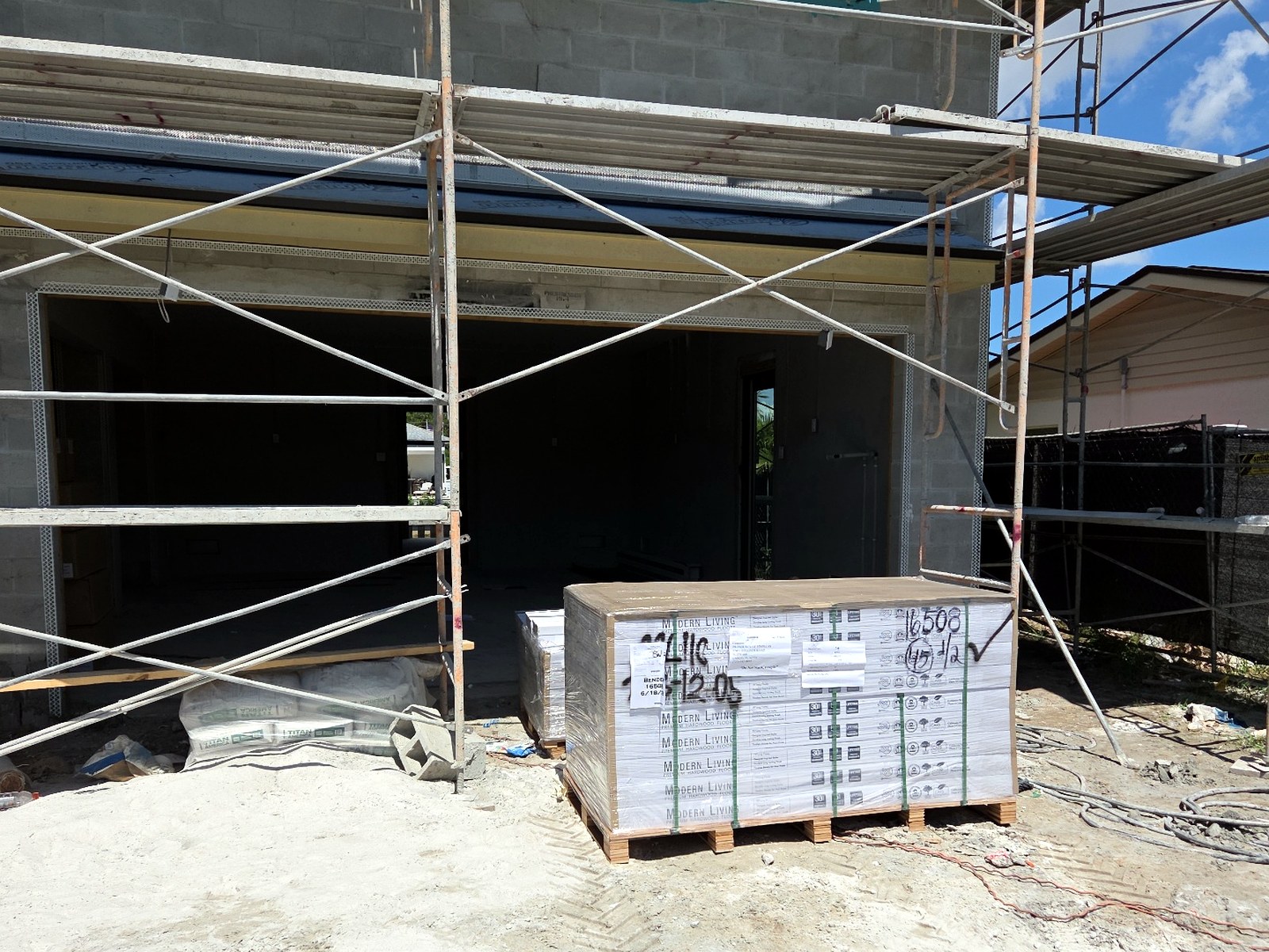 Pallet of flooring delivered and placed at the entrance of an active home construction site with scaffolding
